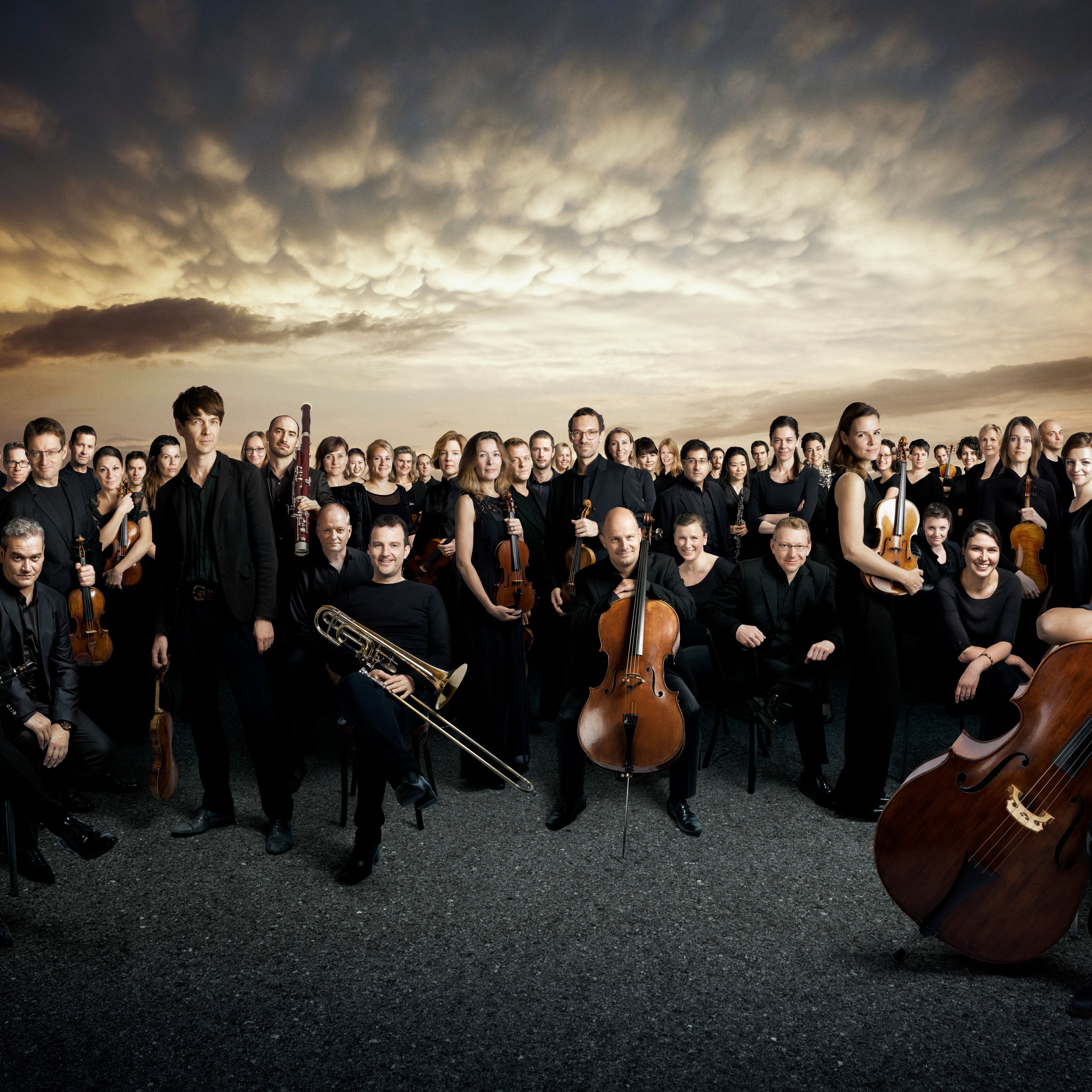 Group picture of the orchestra in front of a dramatic sky