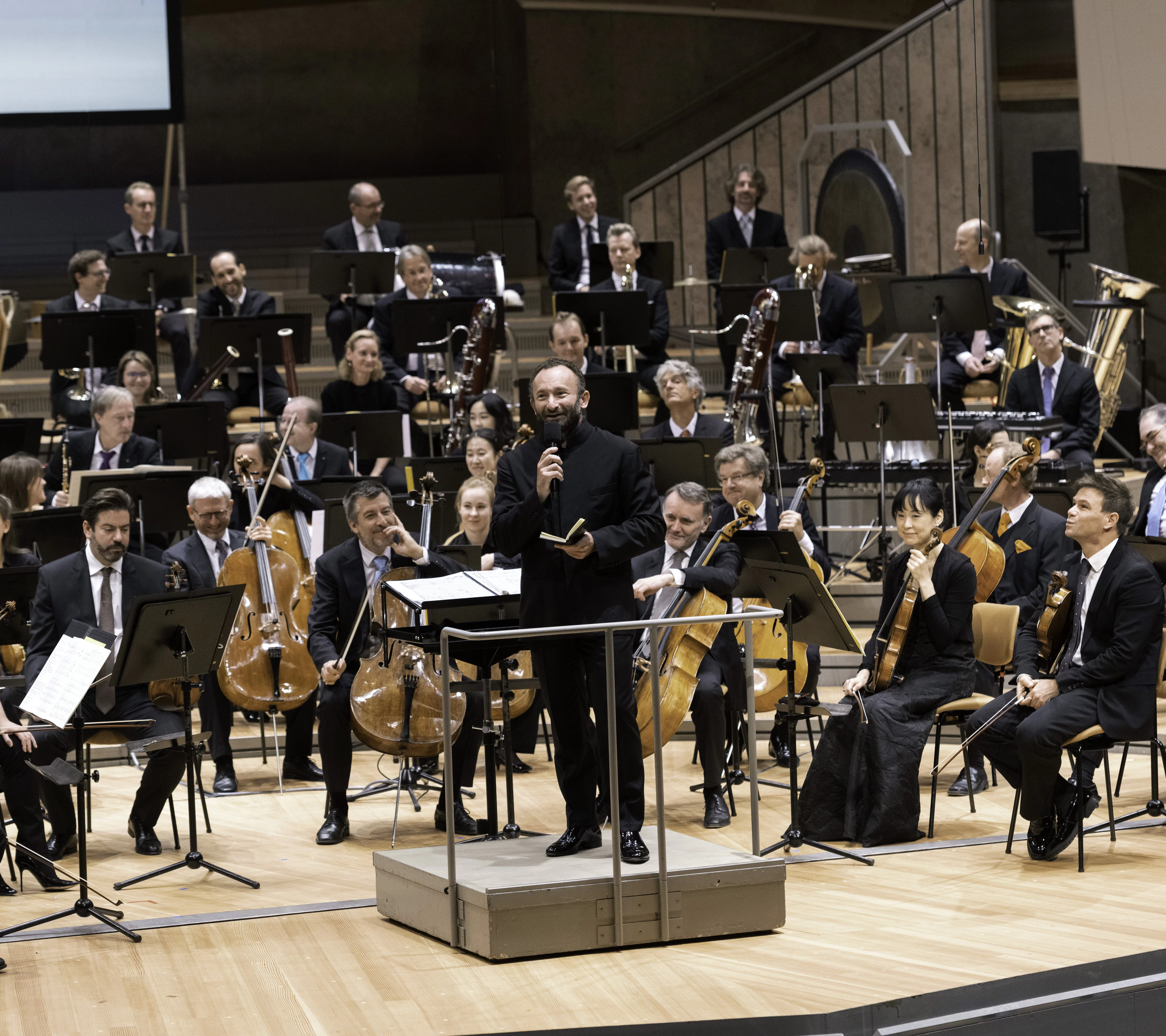 Kirill Petrenko mit Mikrophon vor dem Orchester