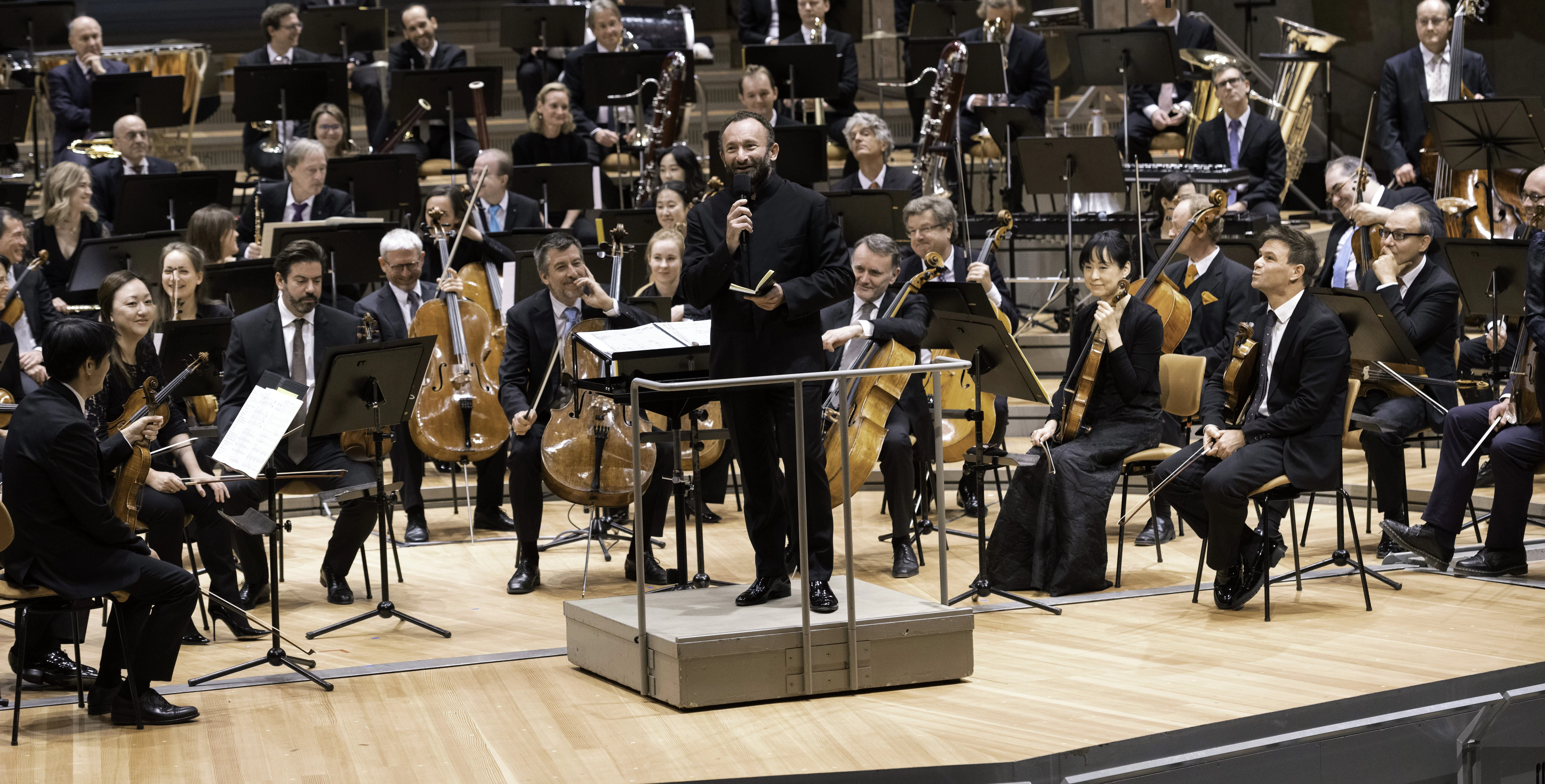 Kirill Petrenko mit Mikrophon vor dem Orchester