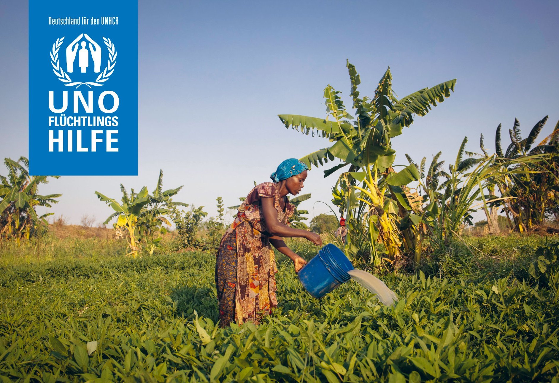 Dieses Bild zeigt eine Frau, die Pflanzen in einer grünen Umgebung gießt, umgeben von Bananenbäumen, mit dem Logo von "UNO Flüchtlingshilfe" (Deutschland für den UNHCR) oben links.