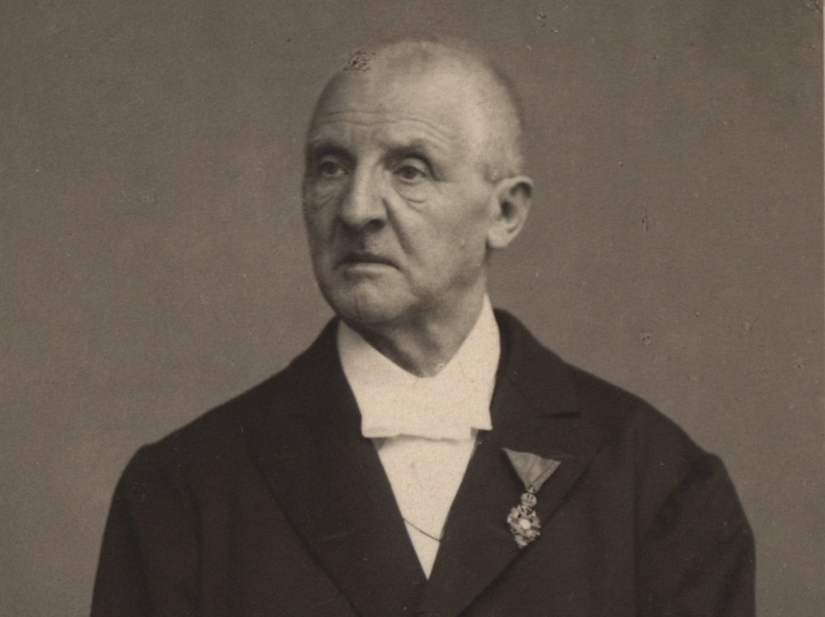 Porträt-Foto von Anton Bruckner. Er blickt zur Seite und hält Dokumente in seiner Hand.