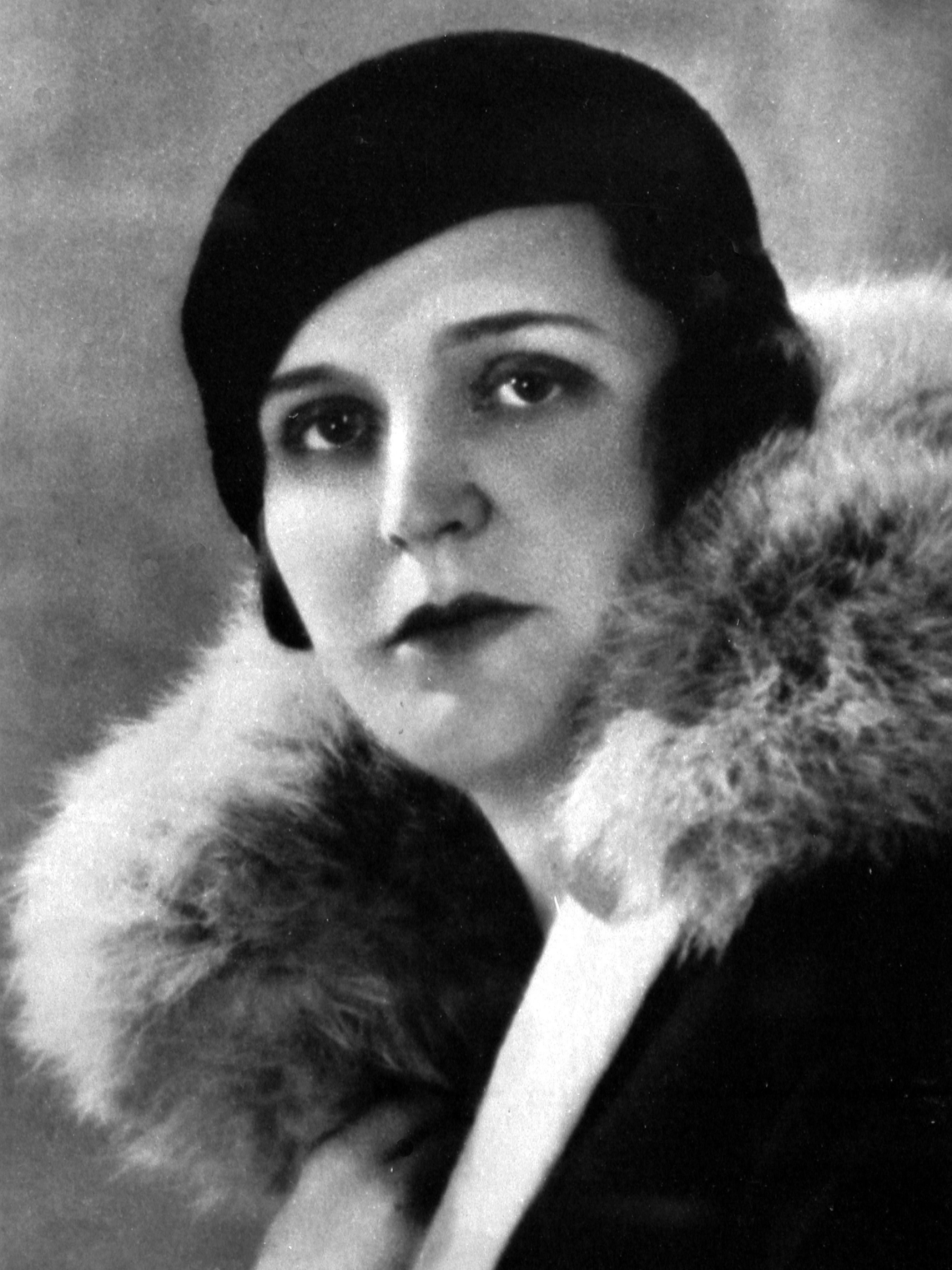 Black and white portrait of Germaine Tailleferre. She is wearing a dark hat and a coat with a lavish fur collar. Her expression is serious and she is looking directly into the camera.