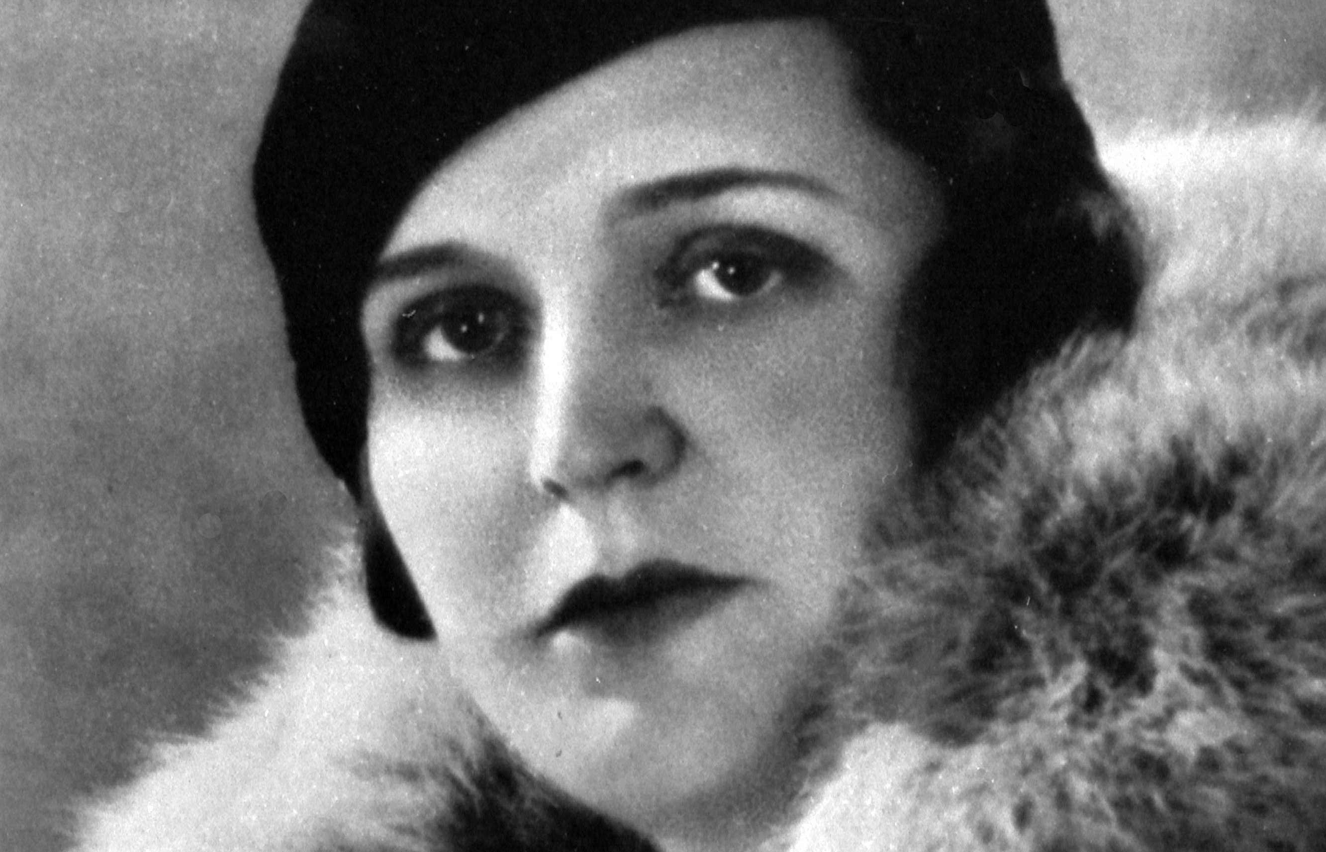 Black and white portrait of Germaine Tailleferre. She is wearing a dark hat and a coat with a lavish fur collar. Her expression is serious and she is looking directly into the camera.