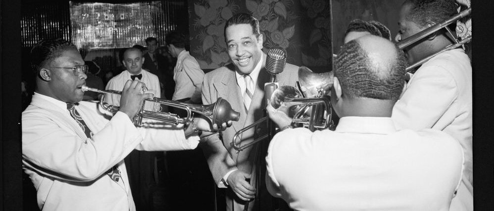 Vier Personen mit Instrumenten spielen auf einen frontal den Betrachtenden zugewandten Mann mit Mikrofon zu.