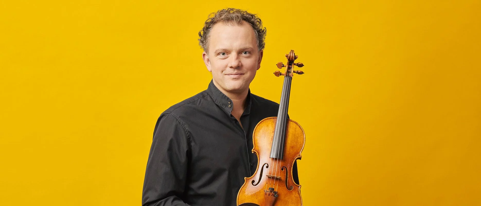 Porträt vor gelbem Hintergrund. Philipp Bohnen hält seine Geige in der Hand.