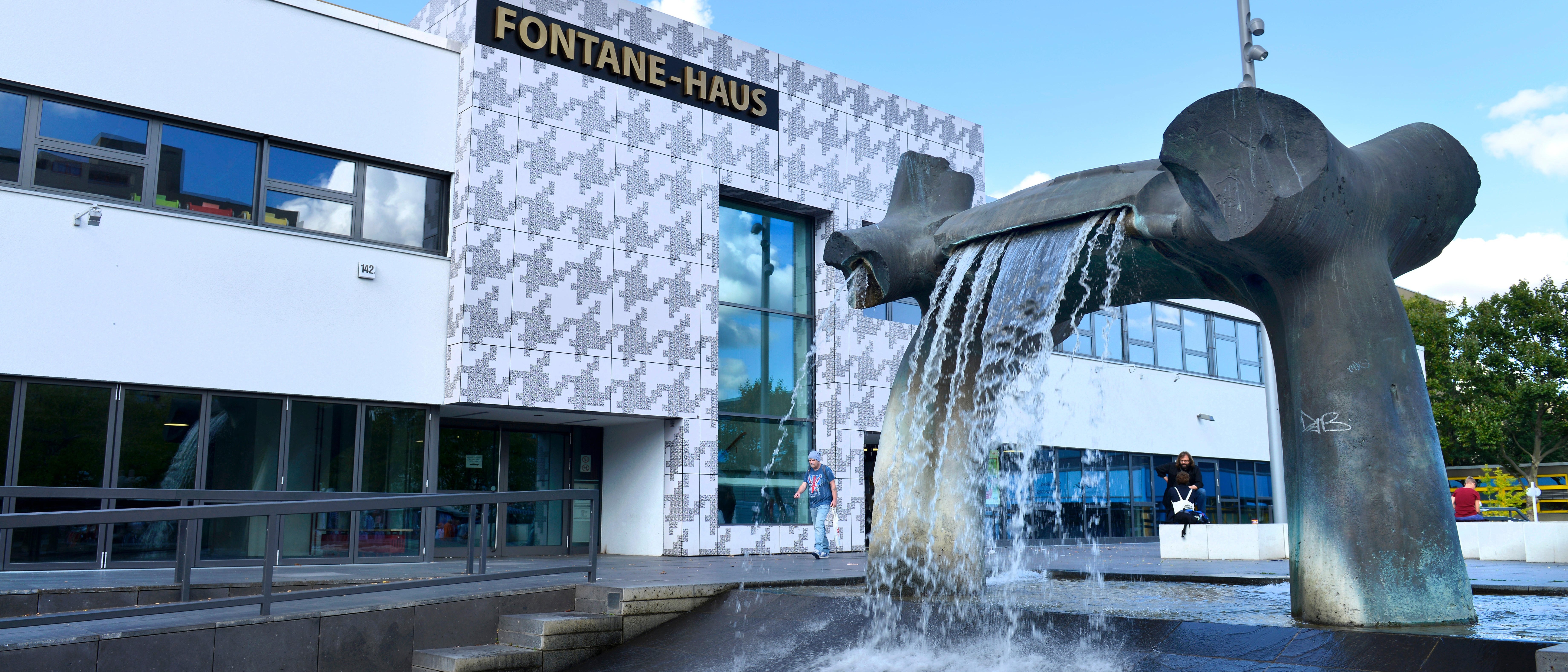 ChatGPT   The picture shows the Fontane House in Berlin, a modern building with a white façade and pattern. In the foreground is a large, sculptural fountain with waterfalls that dynamically enlivens the scene. 