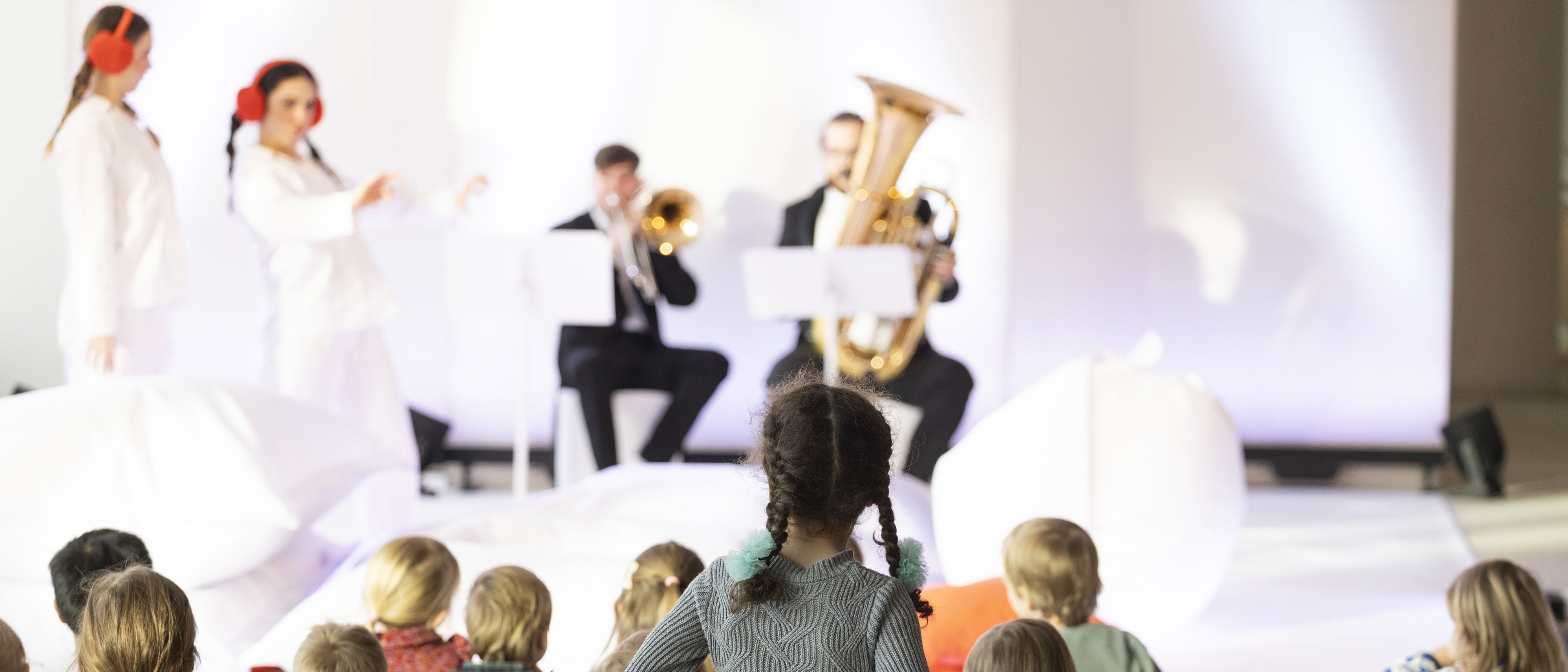 Kinder im Publikum, zwei Musiker spielen Musik, zwei Frauen in weißen Anzügen