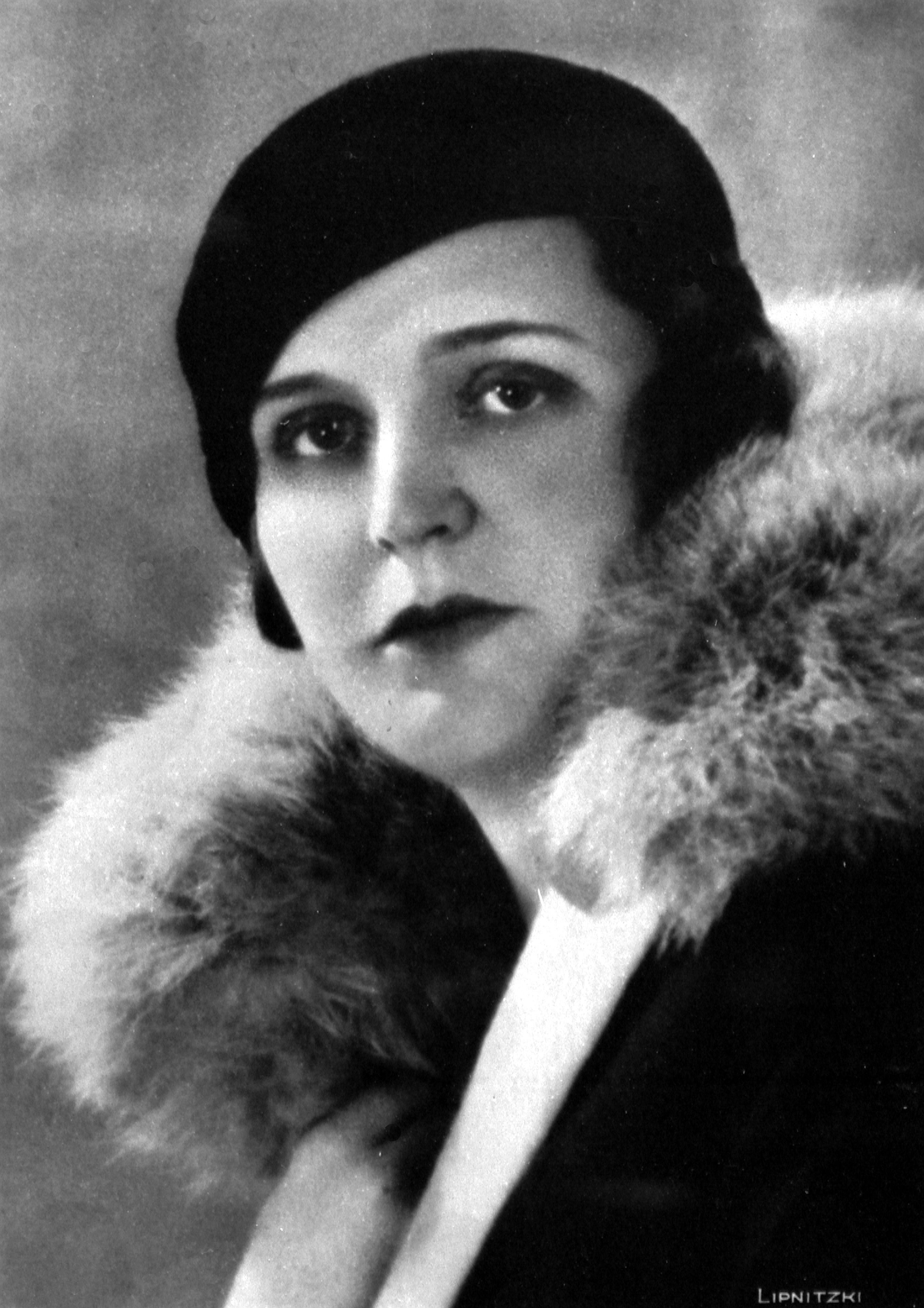 Black and white portrait of Germaine Tailleferre. She is wearing a dark hat and a coat with a lavish fur collar. Her expression is serious and she is looking directly into the camera.