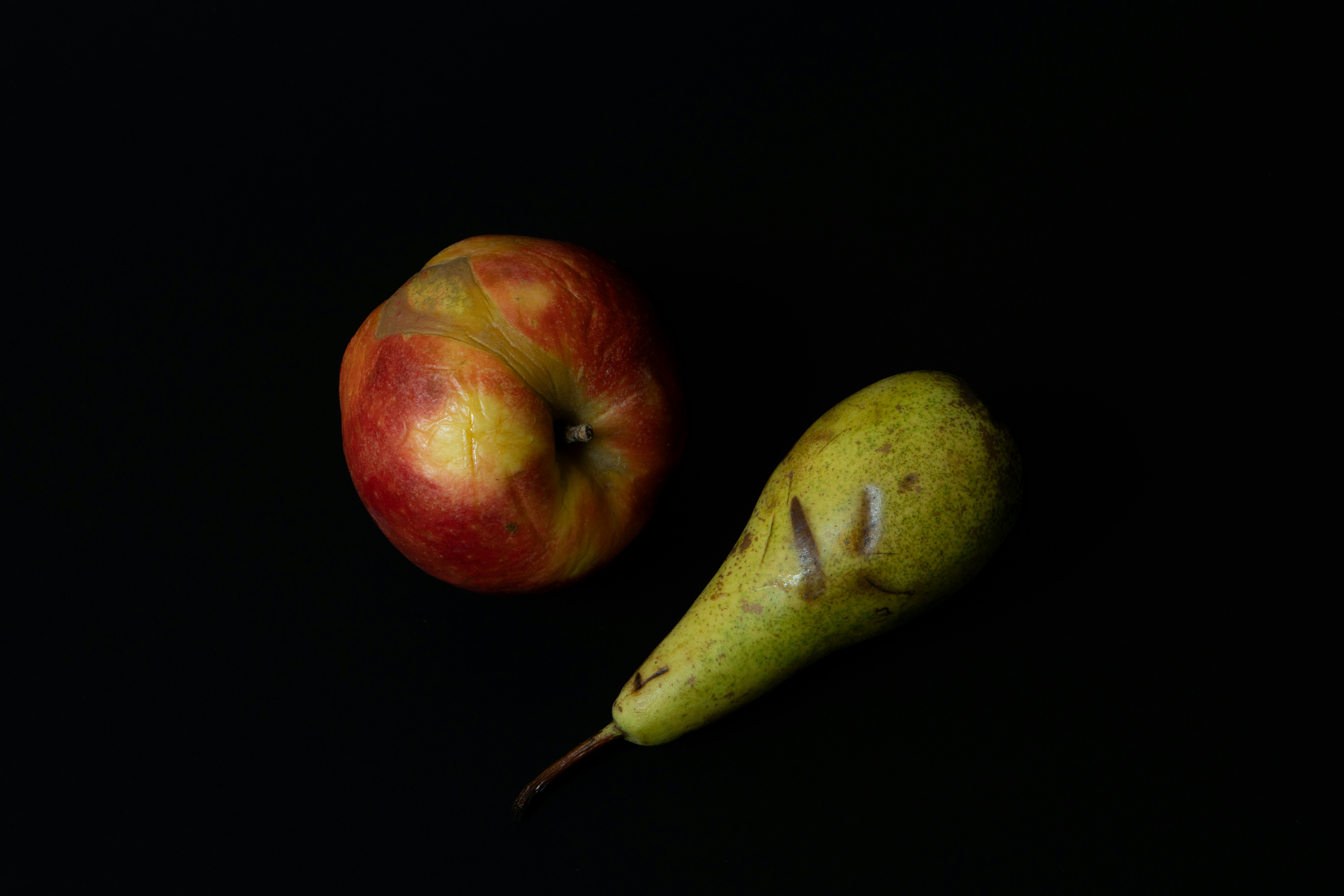 An apple and a pear lie on a black background