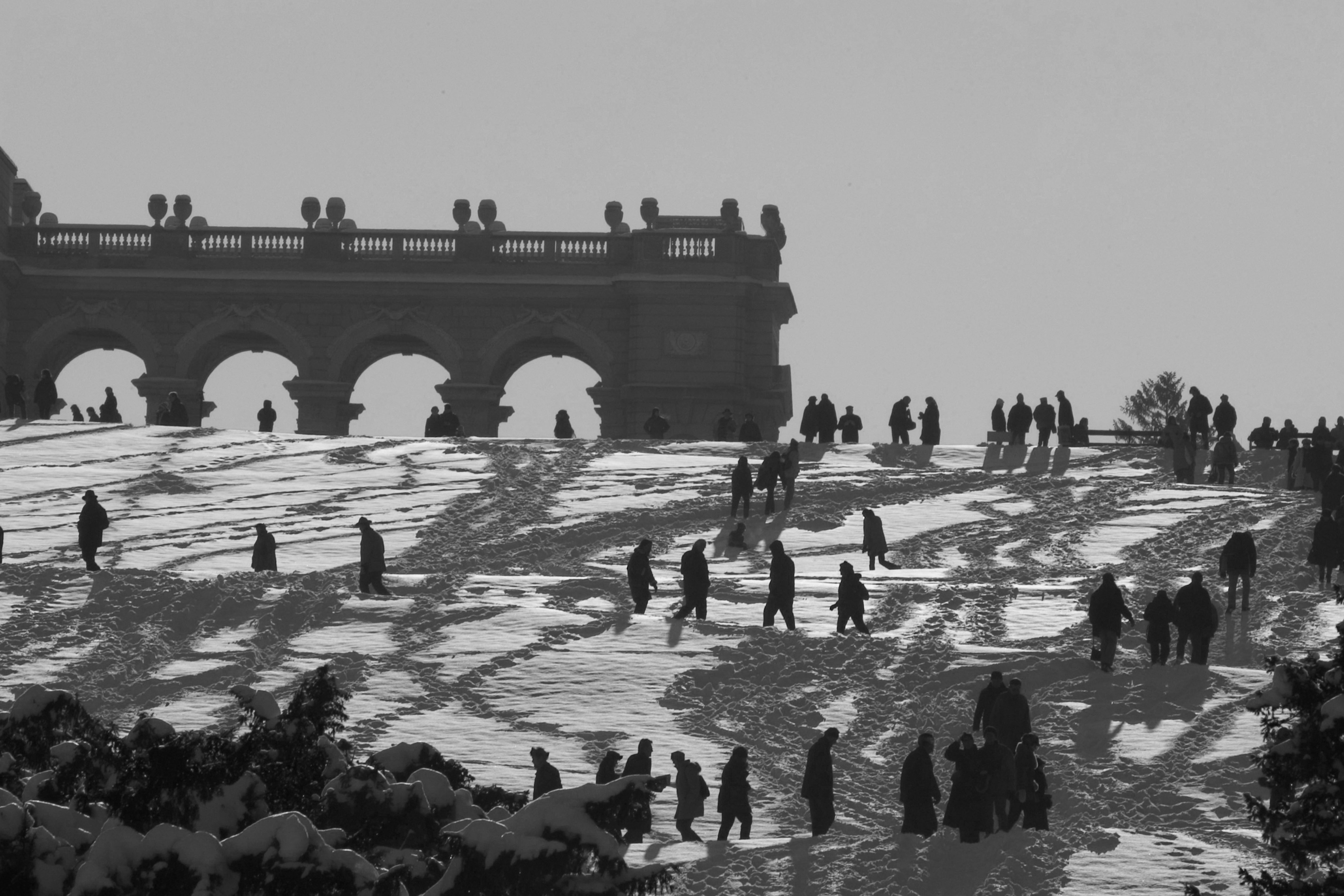 People walk in the snow up a hill crowned by baroque architecture.