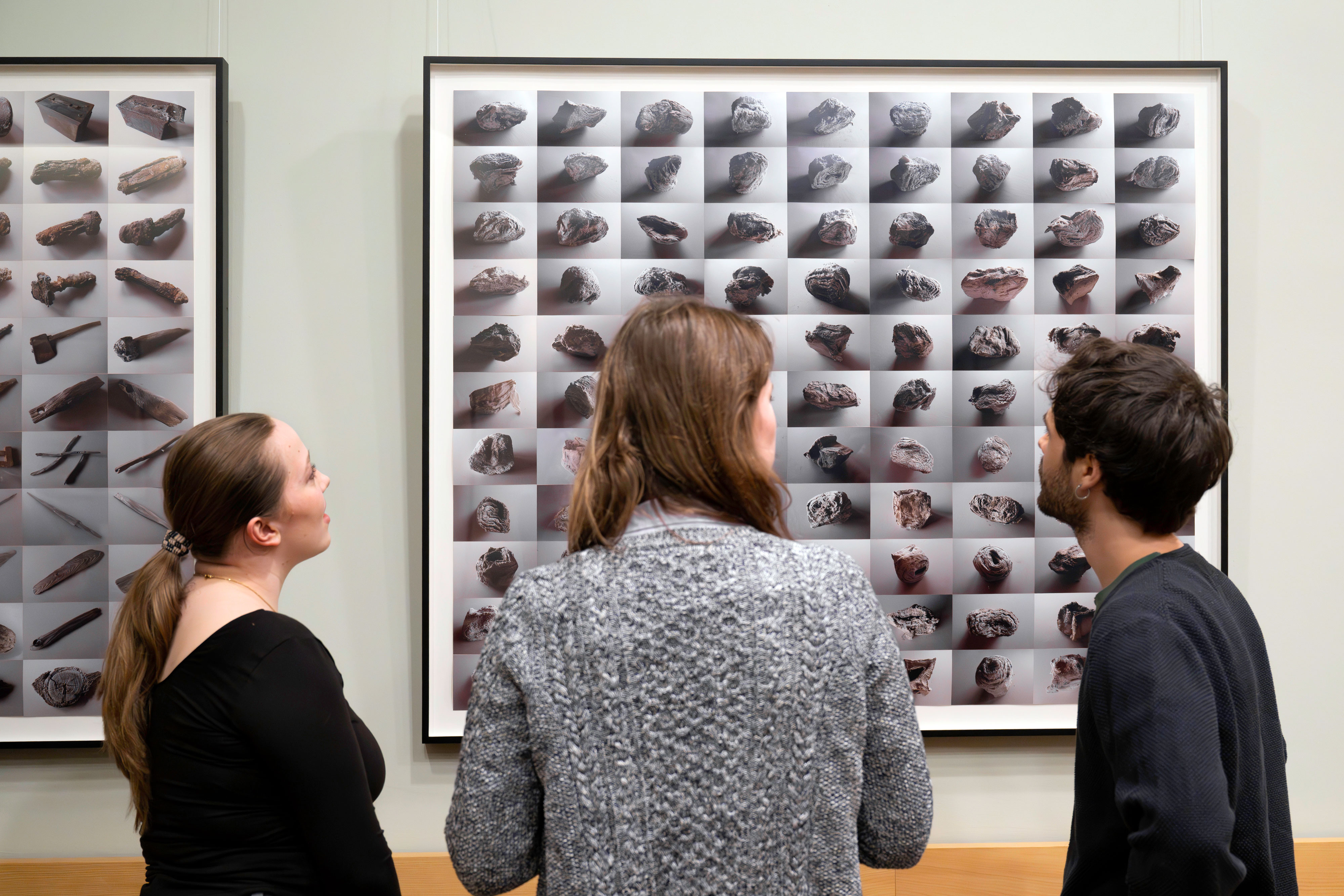 In an exhibition, three people look at large-format photographs that show various objects or structures in grid form.